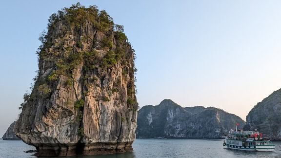 Malá výletní loď s turisty v blízkosti velkého skalního útvaru a turistické atrakce v zátoce Halong ve Vietnamu, jihovýchodní Asie