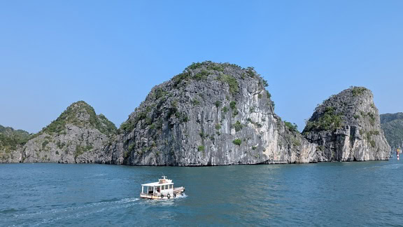 Kis turistahajó a vízben egy nagy sziklaképződménnyel a Halong-öbölben, Vietnamban, Délkelet-Ázsiában