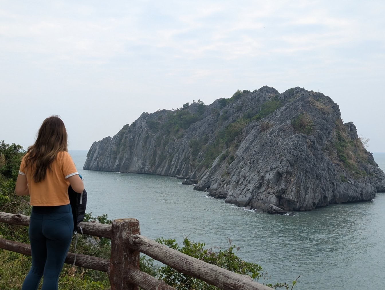 Žena stojící u plotu na vyhlídce a s výhledem na mořskou krajinu s ostrovem, zátoka Halong, Vietnam