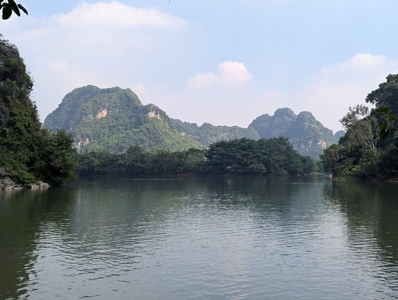 Klidná jezerní voda se stromy a horami v pozadí, severní Vietnam, jihovýchodní Asie