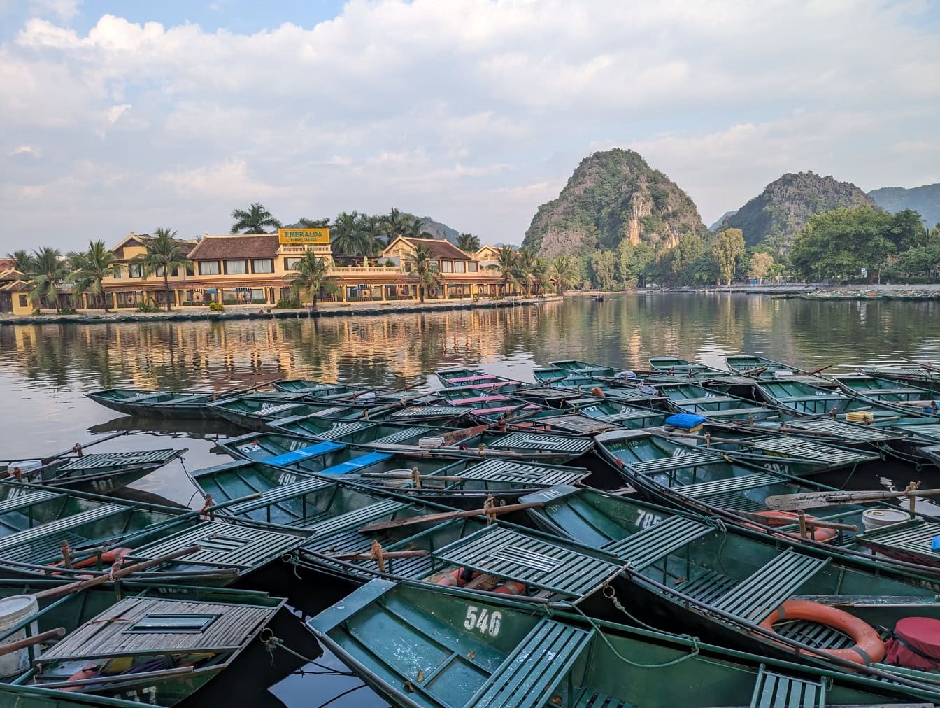 Panoraama järven rannalla pienillä veneillä telakoituna Emeraldan lomakohteeseen Tam Coc Trang Anissa lähellä Ninh Binhin kaupunkia, joka on Unescon perintökohde Vietnamissa