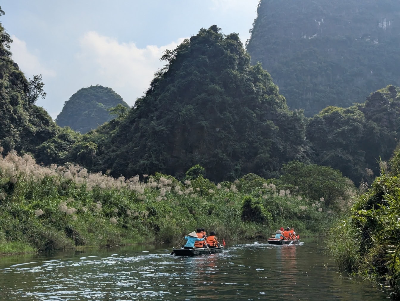 Turistit pienissä veneissä joella, jonka taustalla on vuoristoviidakko, ekomatkailu Pohjois-Vietnamissa, Kaakkois-Aasiassa