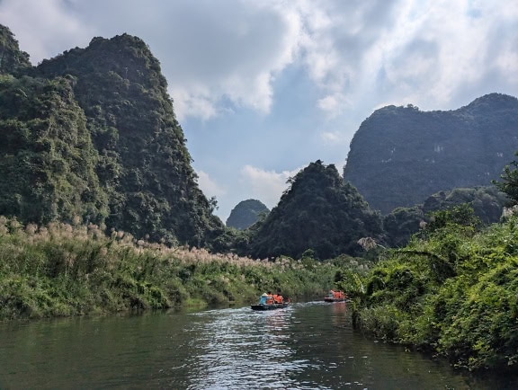 Ekoturistika ve volné přírodě, lidé pádlující na lodích po řece Ninh Binh obklopené horami v severním Vietnamu