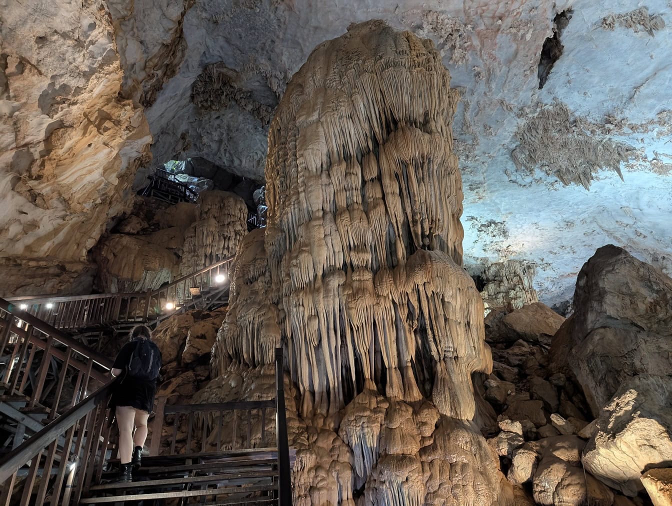 Person walking up a staircase in a cave next to a megalithic mineral formation made of stalactites and stalagmites in the Paradise cave, Vietnam