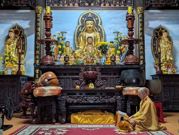 A Buddhist monk kneeling and praying in front of a statue inside a shrine of a Buddhist temple, Vietnam