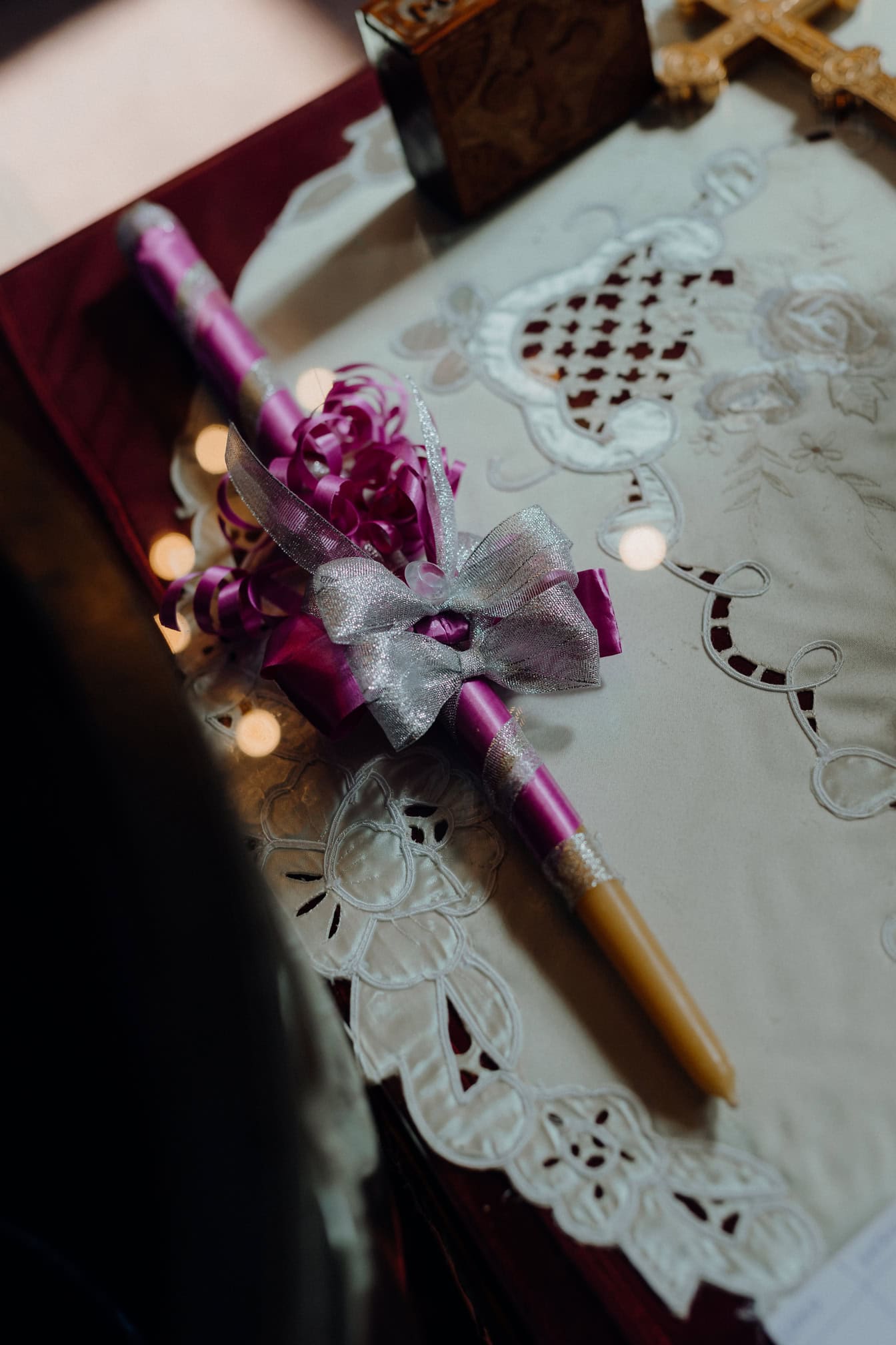 A candle with a fancy purple bow on a table, a religious candle used during coronation or baptism ceremonies