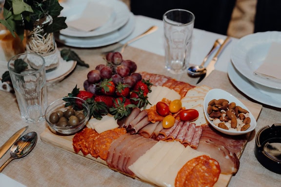 A plate with slices of pork loin, homemade sausage and cheese with fruit, a delicious appetizer on a lunch table