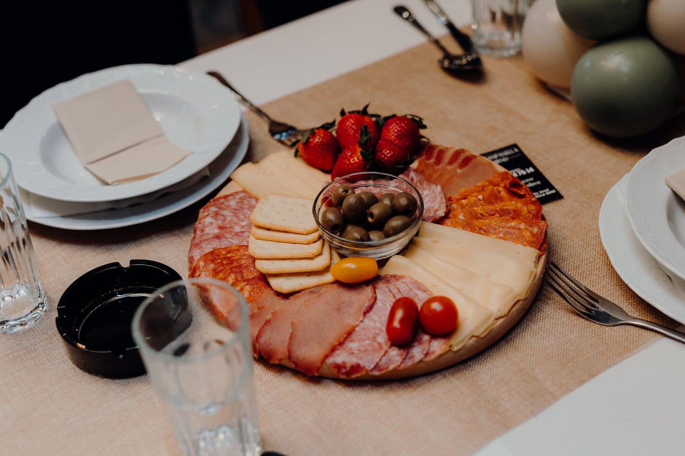 A table with round platter of delicious homemade sausage, pork loin and cheese decorated with olives