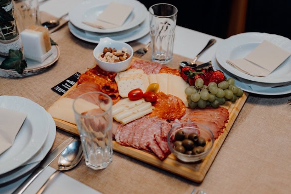 A table set for breakfast with platter of homemade sausage, cheese and pork meat with olives, grapes and strawberries