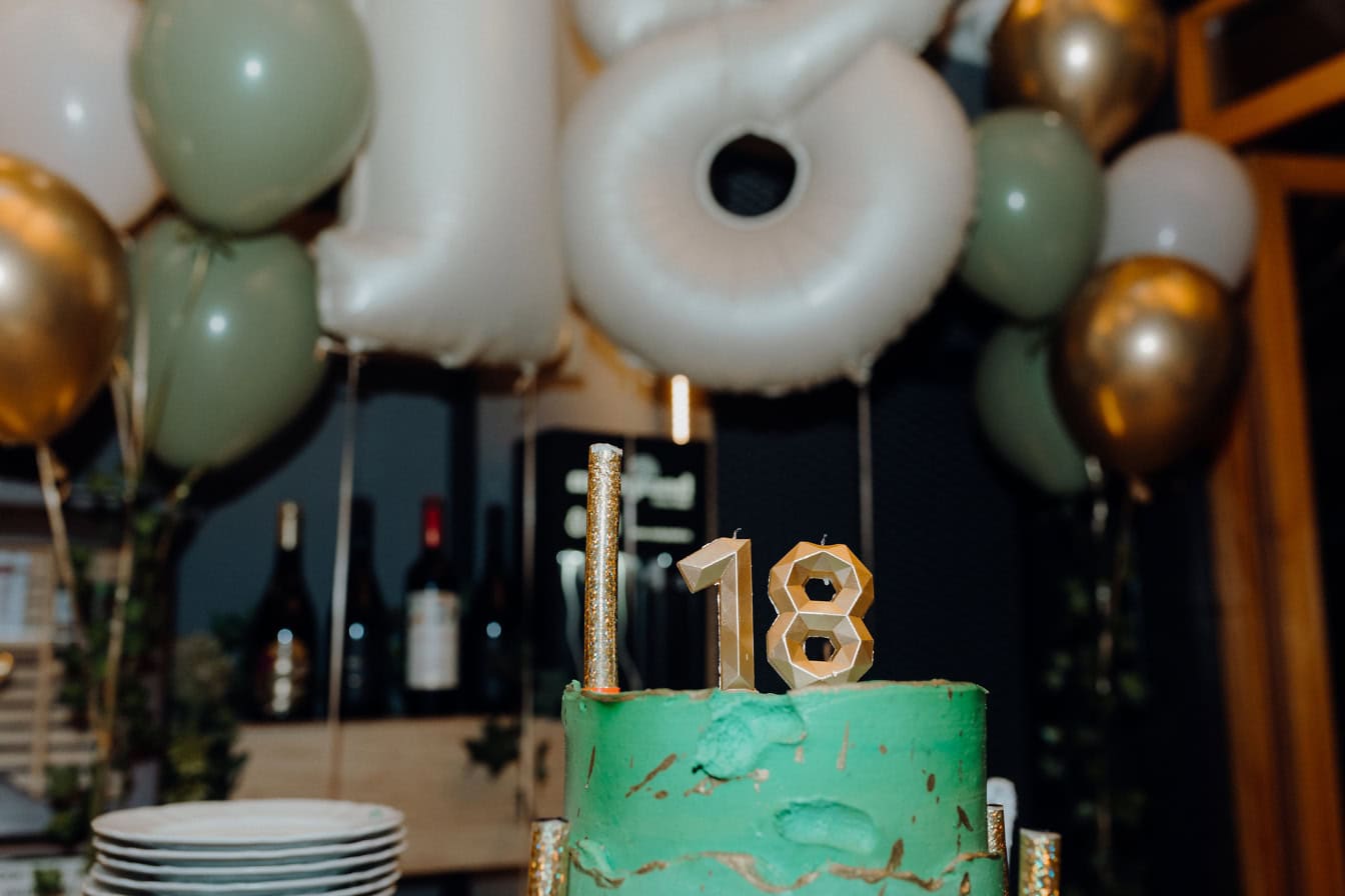 Green birthday cake with candles on a shape of gold number eighteen (18) on top of cake