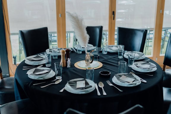 A fancy black dining room table with plates and cutlery, an elegant lunch table with black chairs