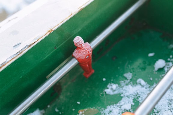 A table soccer, a frost on a red plastic figurine on a metal bar of a table football