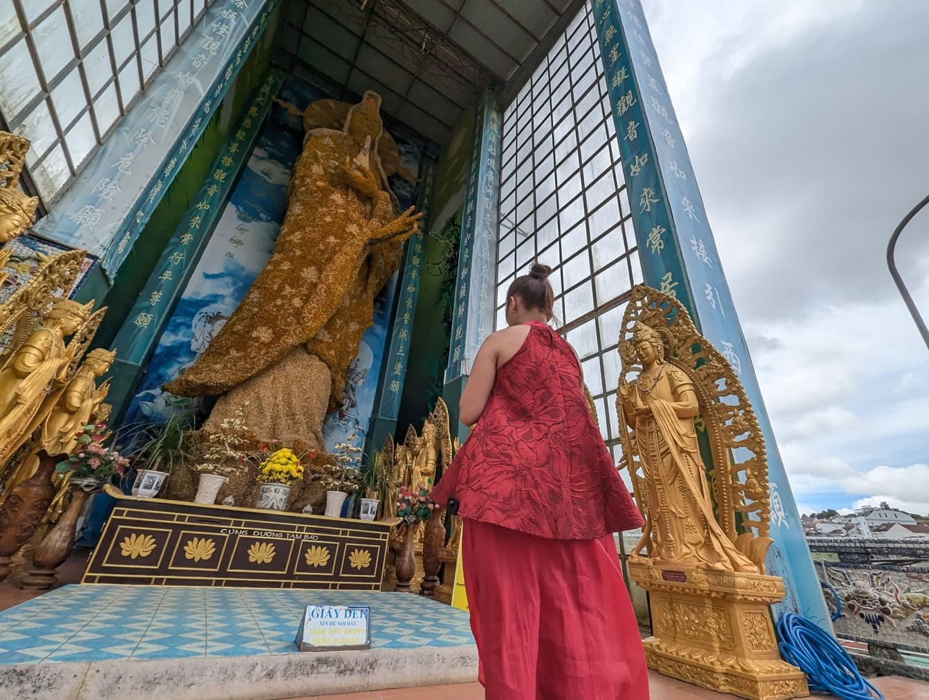 Žena v červených šatech stojící před pagodou Linh Phuoc, buddhistickým skleněným chrámem z porcelánu s největší sochou bódhisattvy Avalókitéšvary na světě, Da Lat, Vietnam