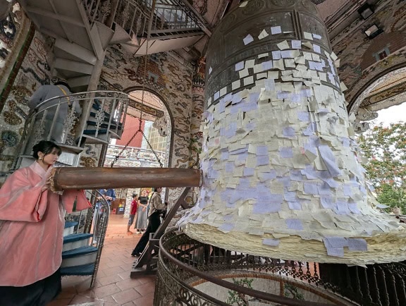 Buddhistická žena bijící do velkého litinového zvonu s mnoha papírovými samolepkami, Pagoda Linh Phuoc nebo Chua Linh Phuoc, Dalat, Vietnam