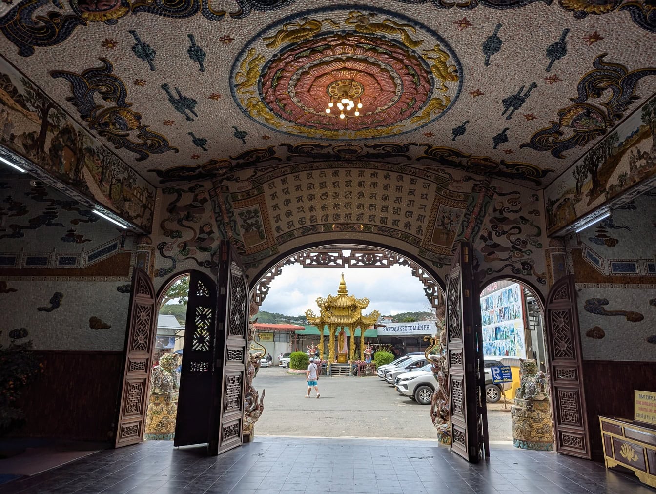 Koristeltu katto mosaiikilla ja holvikäytävällä, josta on näkymät Linh Phuocin buddhalaiselle pagodille, jossa on iso kultainen Buddhan patsas, Vietnam