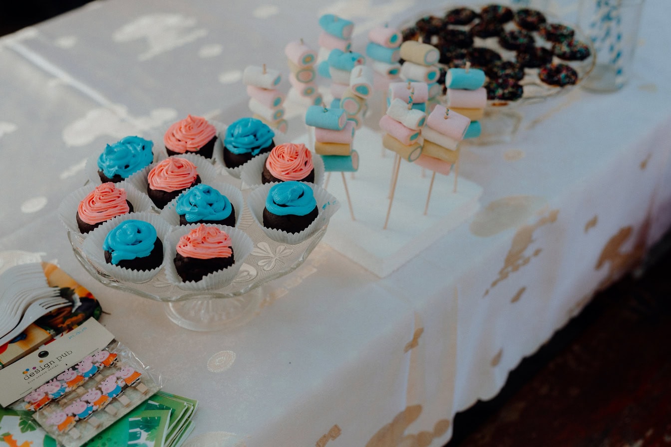 Une table avec des desserts dessus, des cupcakes au chocolat avec un glaçage bleu et rosé, des sucettes, des bonbons et d’autres délicieuses confiseries