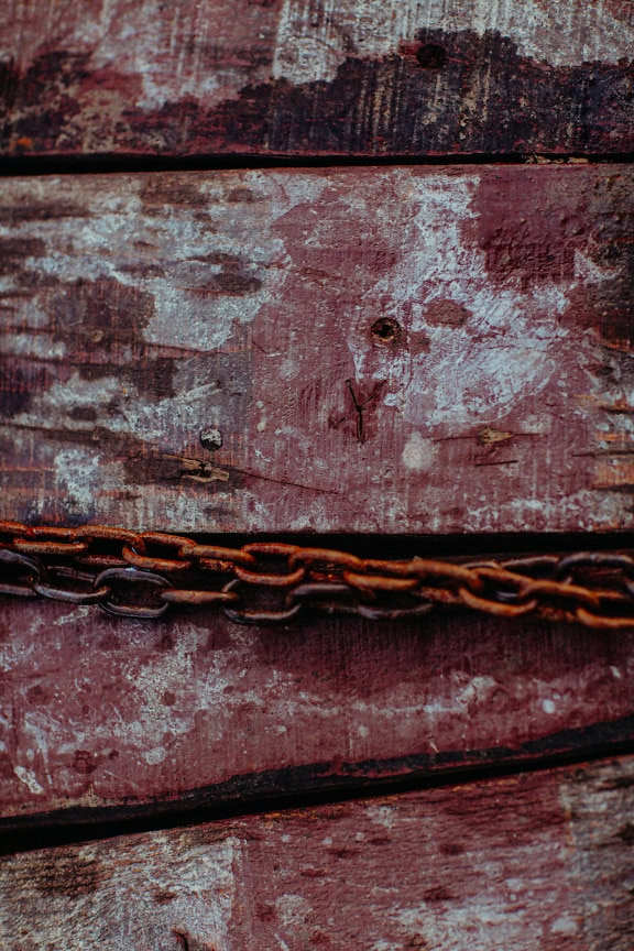 Close-up of an old rusty chain on a dirty wooden planks, a texture of rough wood surface painted with reddish-brown paint