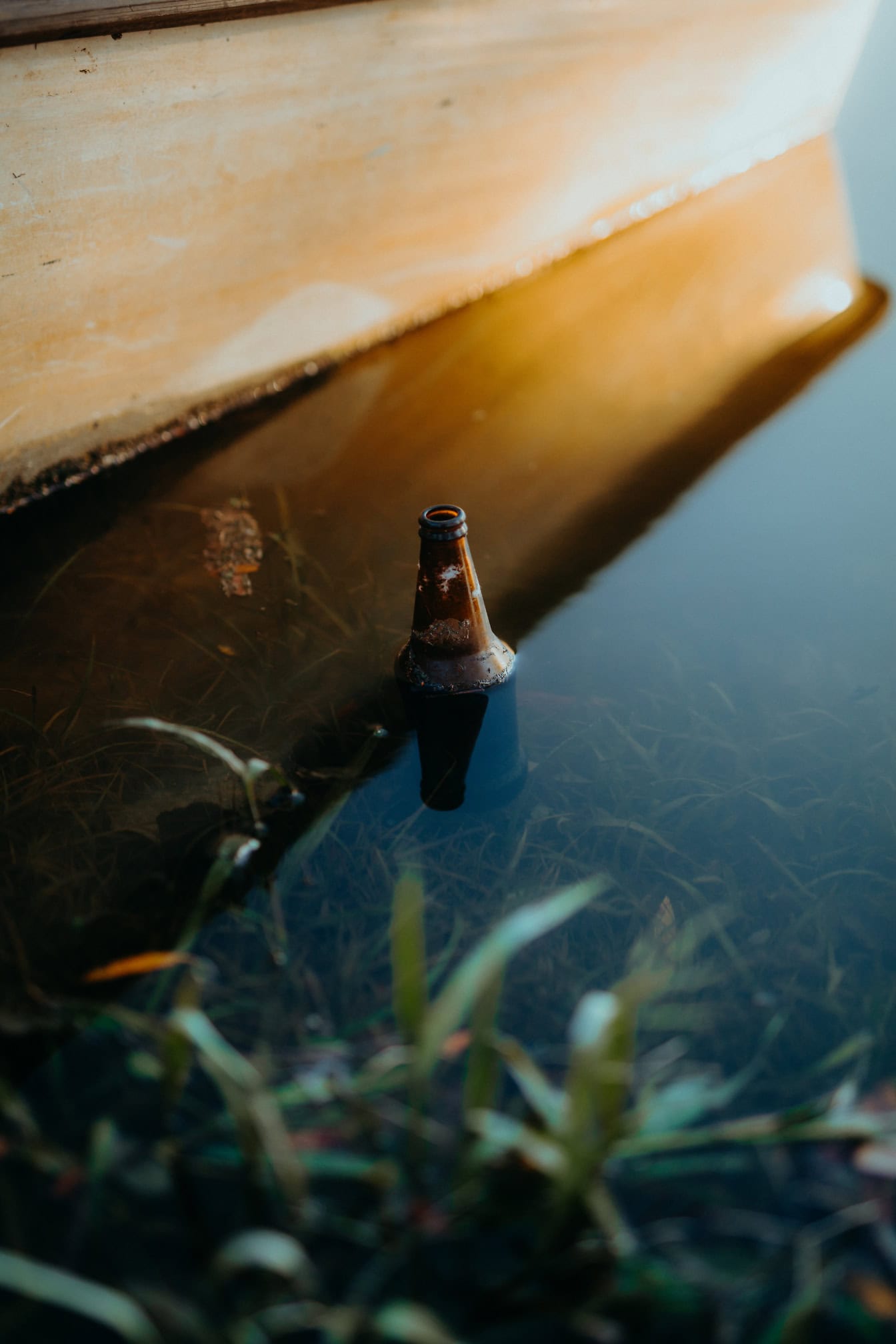 Vieja botella de vidrio marrón desechada en el agua, contaminación del agua por desechos de vidrio