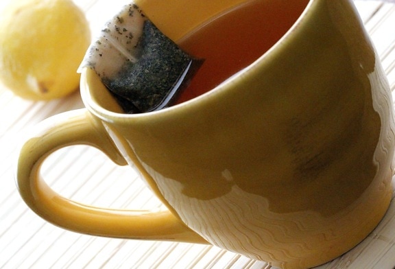 yellow, ceramic, cup, contained, hot, water, resting, rim, steeping, tea, bag