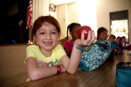 miling, young girl, foreground, holding, red, delicious, apple, hand
