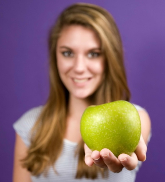 young woman, extending, arm, holds, green, Granny Smith apple